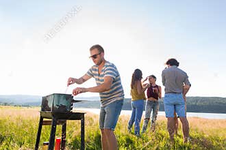 Clique of young people making BBQ at lake