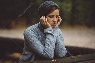 Portrait of sad woman sitting alone in the forest. Solitude concept. Millenial dealing with problems and emotions.