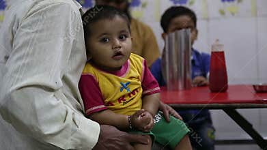 Portrait of Indian baby held by a parent, with another child in background.