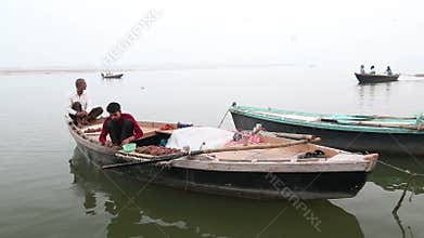 Two men sitting in boat on Ganges, while boats sail in background.