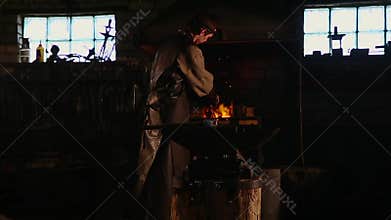 Blacksmith brings dripping hot metal from furnace and creates a shower of sparks as he beats a piece of white hot metal