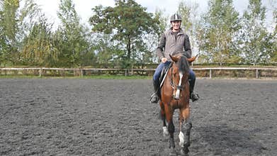 Young man horseback riding outdoor. Male jockey at horse walking at manege at farm on dark cloudy day. Beautiful nature