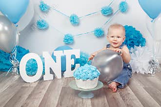 Caucasian baby boy in dark pants and blue bow tie celebrating his first birthday with letters one and balloons