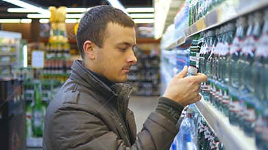 Young man choosing and buying bottle of mineral water at the supermarket. Guy taking product from shelves at grocery
