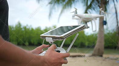 Man Controls Flying Quadcopter Via Remote Control with Tablet Gadget Screen. Drone Pilot Practice Flight on the Beach.