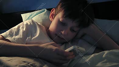 Boy resting in his bed in the evening and using his smart phone