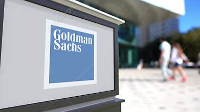 Street signage board with The Goldman Sachs Group, Inc. logo. Blurred office center and walking people background
