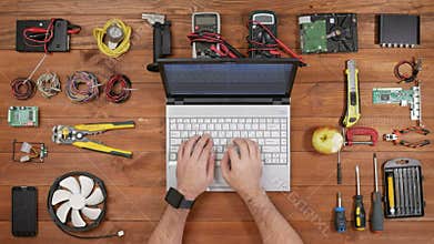 Male engineer software typing at his laptop and eating apple. Wooden table for electronics repair top view