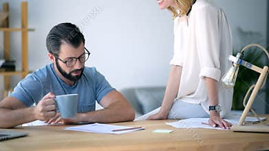Friendly colleague bringing coffee for male freelancer struggling with work