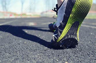 Track athlete image, of person walking on track before practice in the daylight. Shows rubber under feet and hurdles in the back.