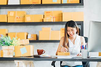 Young Asian small business owner working at home office, taking note on purchase orders. Online marketing packaging delivery