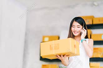Small business owner, Asian woman hold package box, using mobile phone call receiving purchase order, working at home office