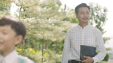 Asian boy walking through garden to school with father back lit in slow motion