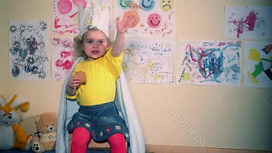 Cute princess girl with paper crown sitting and eating cookie