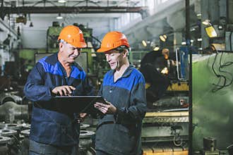 Two workers at an industrial plant with a tablet in hand, workin