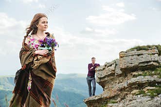 Portrait of a young bride in a colorful dress with a bouquet of wildflowers in the nature standing on the background of