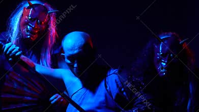 Ninja with a katana and two freaks dressed in a kimono in demon masked with fans pose in the dark in the rays of red