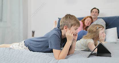 Son bed use tablet computer lying on parents over happy smiling family together in morning