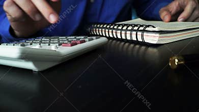 Accountant using calculator and checking in an accounting book.