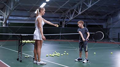 Woman throwing ball while practicing hit with little boy on tennis court