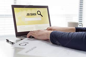 Man trying to find work with online job search engine on laptop. Jobseeker in home office. CV and application paper on table.