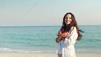 Smiling woman holding heart card at the beach