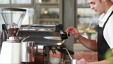 Smiling barista steaming milk at the coffee machine