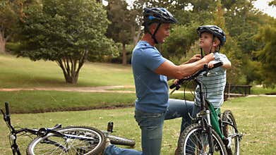 Father attaching his son cycling helmet in the park