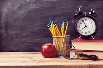 Back to school background with books and alarm clock over chalkboard