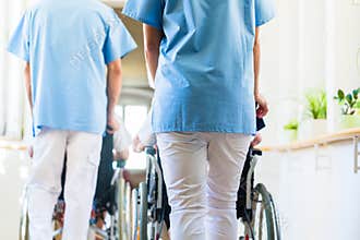 Nurses pushing seniors in wheelchair thru nursing home