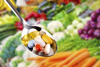 Spoon with pills, dietary supplements on vegetables background