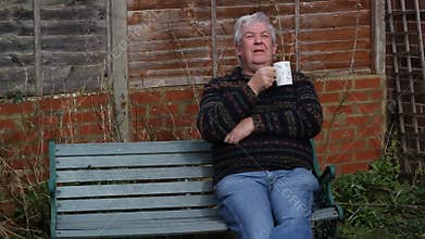 Senior man sitting outside drinking tea or coffee.