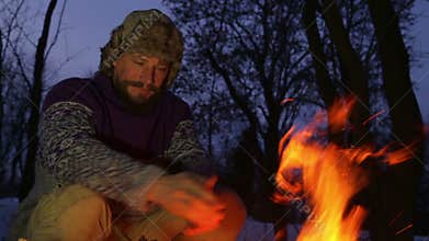 Bearded man warming his hands by the fire in winter. Tourist man evening campfire.