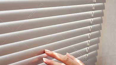 Female hand separating slats of venetian blinds with a finger to see through