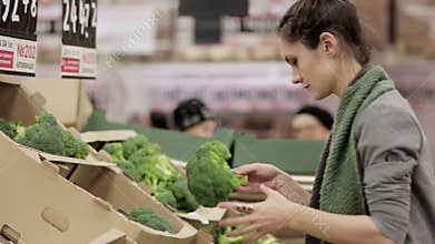 Young woman chooses cabbage on store shelves.