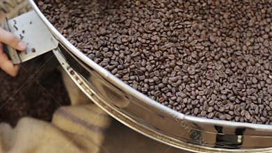 Process pour out of fried coffee grains into bag in factory.