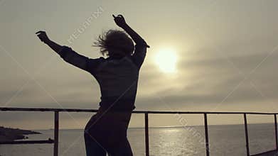 Girl with a figure and short hair incendiary dancing on the pier near the sea at sunset