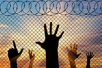 Silhouette refugees hands near the border fence