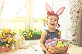Easter. happy child girl with bunny ears and colorful eggs sitting at window in flowers