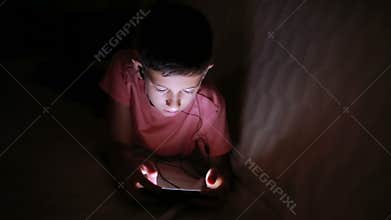 Young boy playing with a cellphone or smartphone on a bed. night