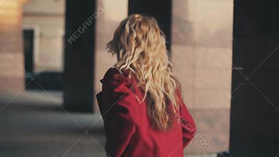 Business woman in red coat goes to business center and looks on watch,she is late for work or meeting.