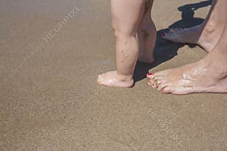 Mother and baby feet walking on sand beach