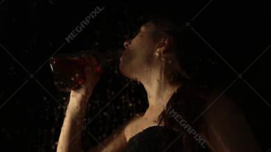 Young sad woman behind the window with drops on it. lonely girl drinking brandy from the bottle and crying