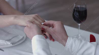 Happy young man making a proposal giving engagement ring to his fiancee in a restaurant ,close up hands