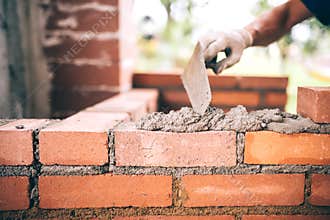 Construction bricklayer worker building walls with bricks, mortar and putty knife