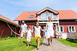 Happy family running on meadow in front of house