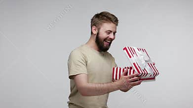 Joyful bearded man slowly opening gift box, unwrapping birthday surprise and expressing great happiness amazement