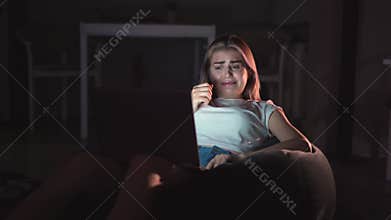 A young woman sits at home alone and watches a horror movie. Cinema online. Favorite movie is always available. A cup of