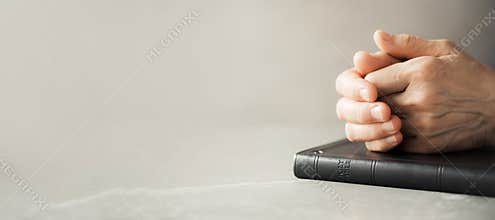 Hands closed in prayer on Holy Bible. Christian banner with copy space. Pray about world during coronavirus Covid-19 pandemic.