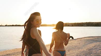 Follow me pov - pretty woman in swimsuit calls boyfriend by hand to swim in lake with her, looking at camera. Back view